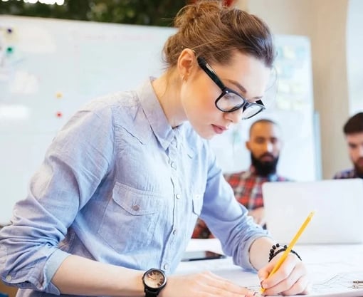 Woman engineer working on blueprint in office with colleagues on background